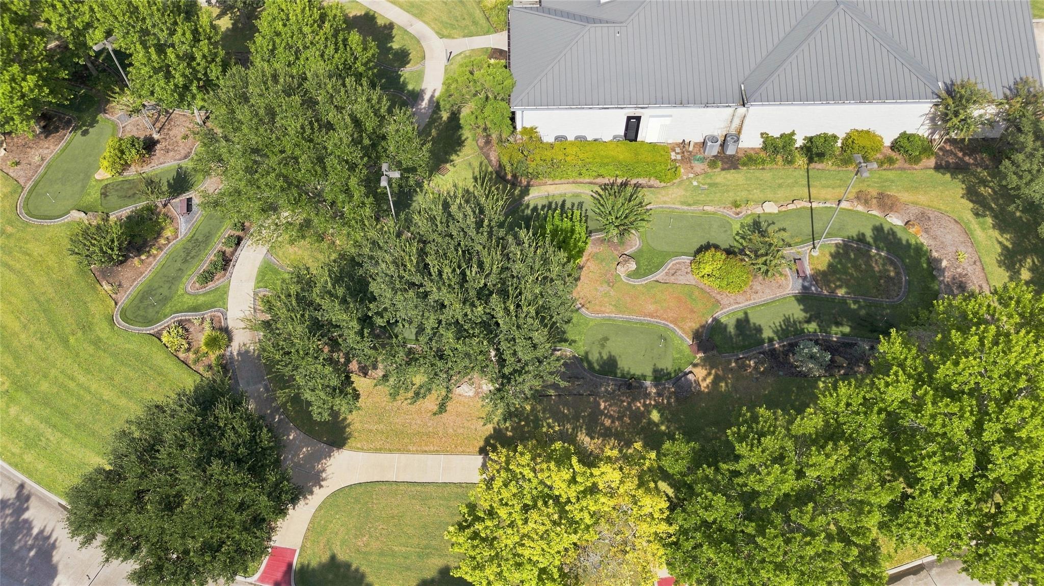 Aerial view of landscaped grounds with putting greens, winding paths, and mature trees beside a large building.