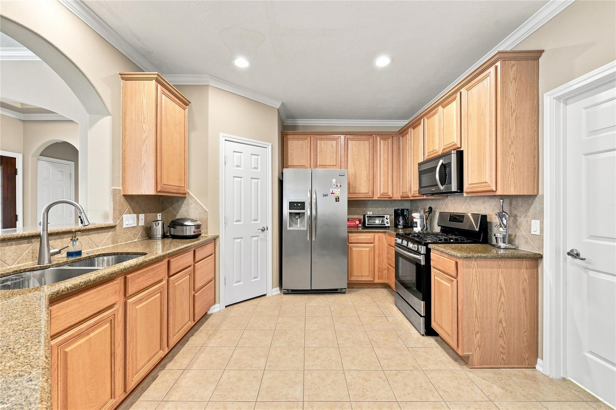 Kitchen with honey-colored cabinets, granite counters, stainless-steel refrigerator and gas range.
