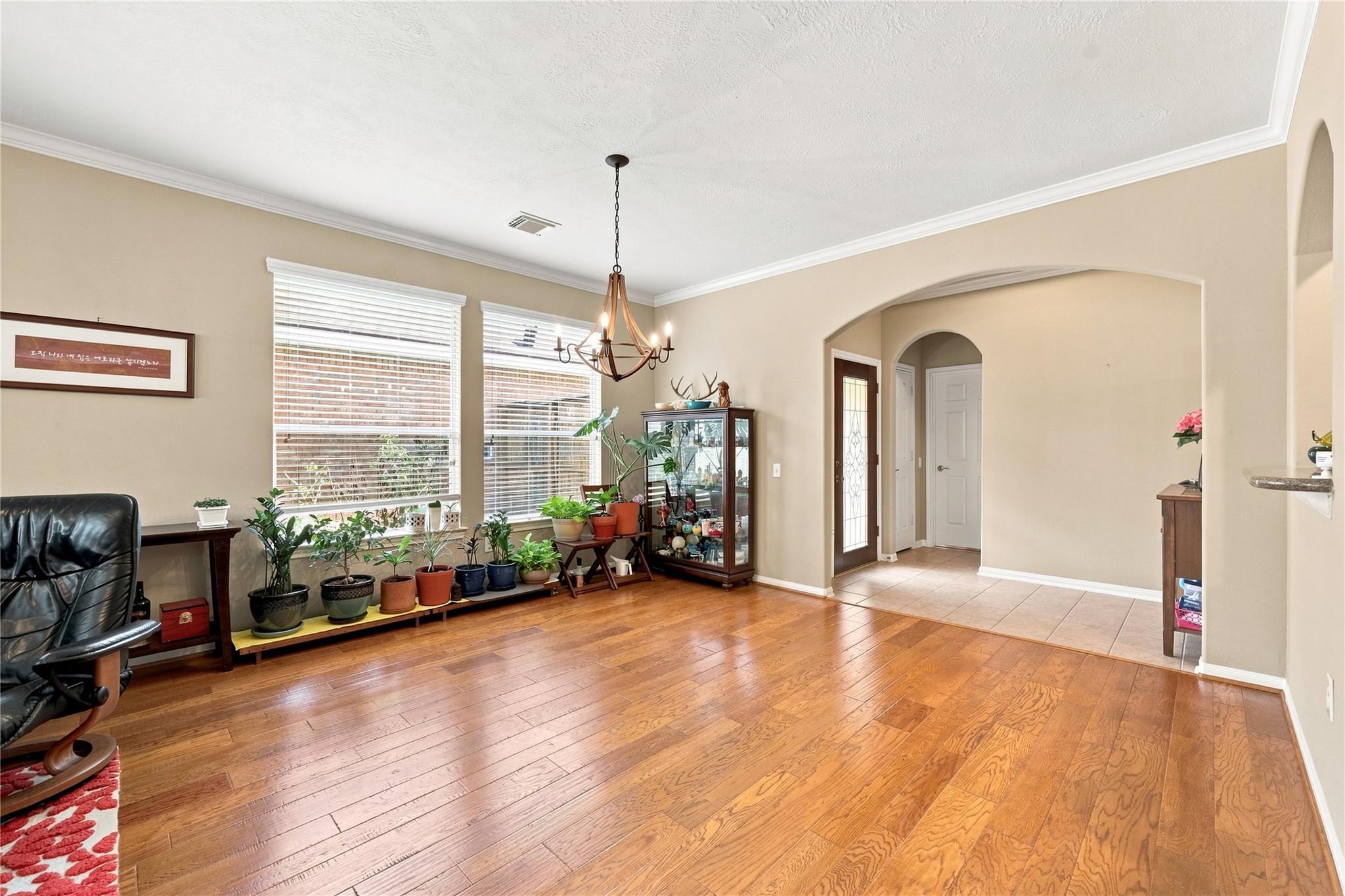 Living room with polished hardwood floors, rows of potted plants beneath two windows, and an arched entryway.
