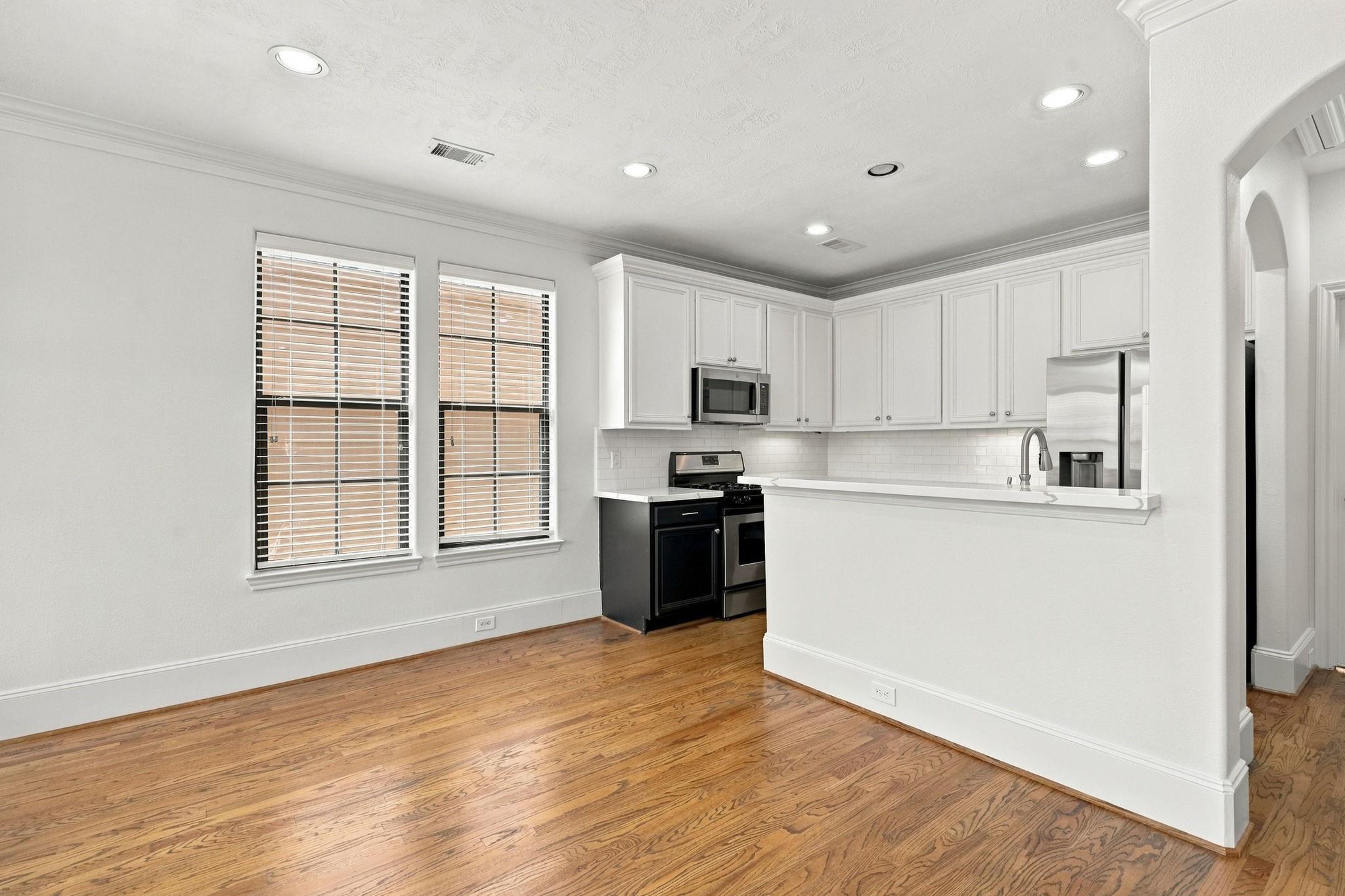 Bright kitchen with white cabinets, stainless steel appliances, breakfast bar, and hardwood floors.