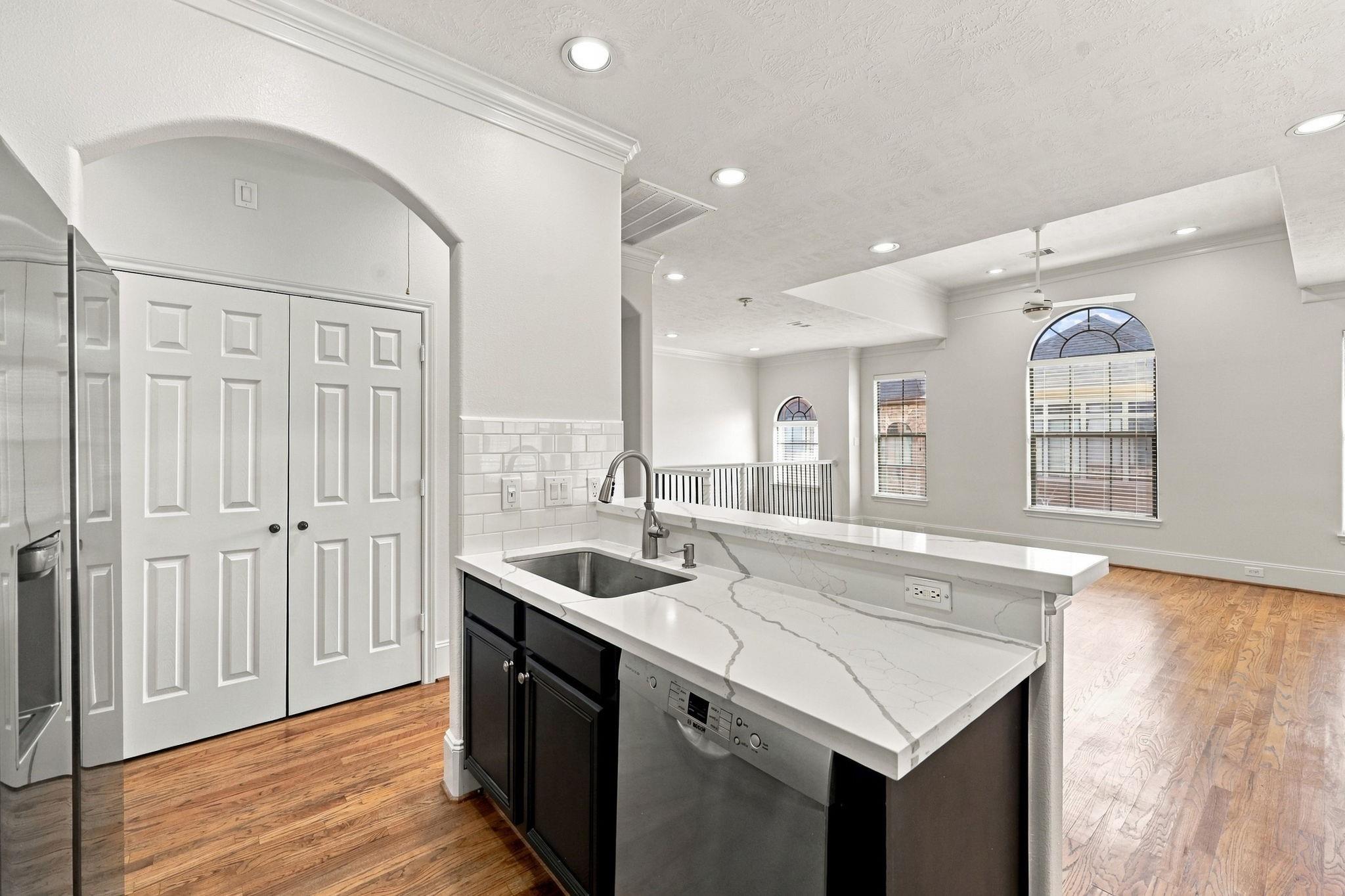 Kitchen with a large veined quartz island, dark cabinets, stainless appliances, and arched windows.