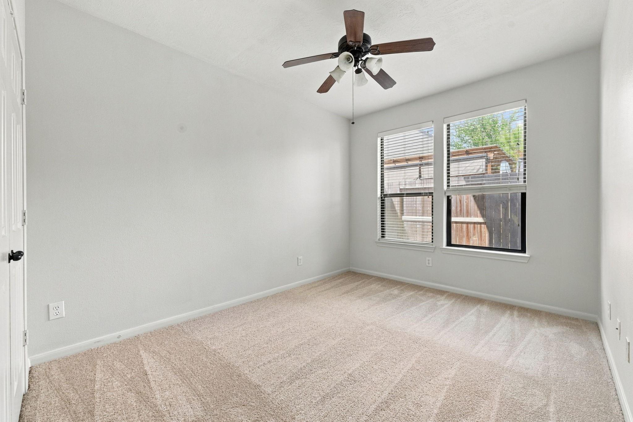Empty carpeted bedroom with two windows and a dark wood ceiling fan.