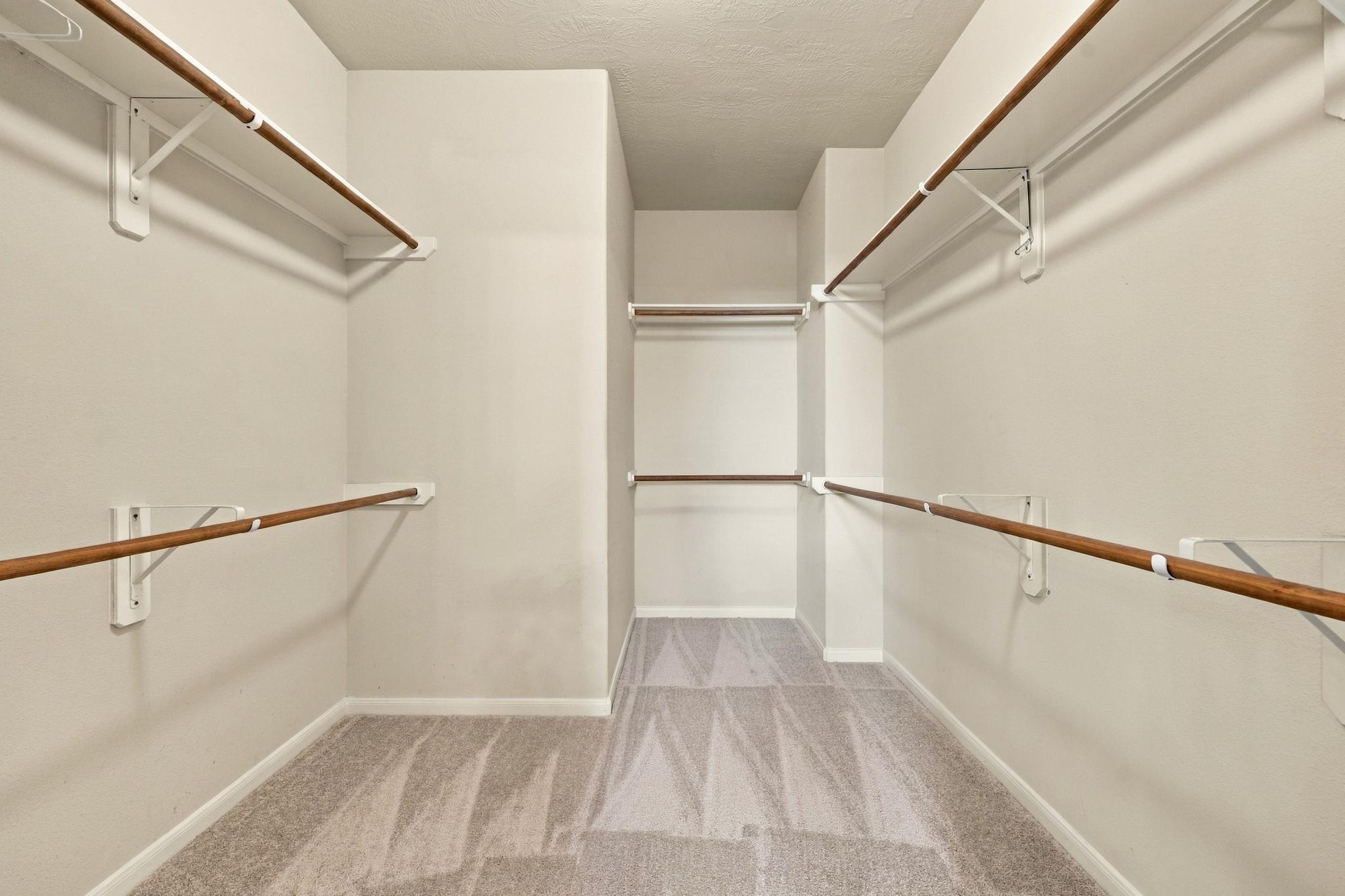 Walk-in closet with wooden clothes rods on three walls and gray carpet.