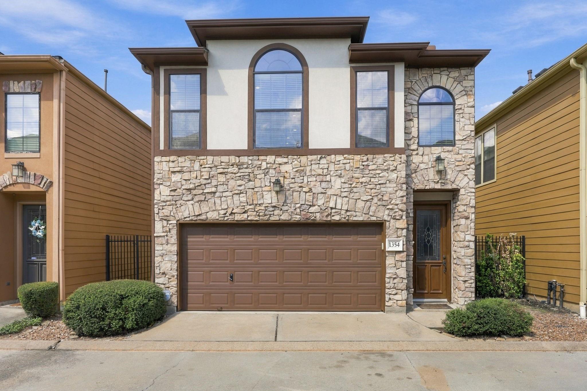 Two-story stone-front home with a brown double garage door and tall arched windows.