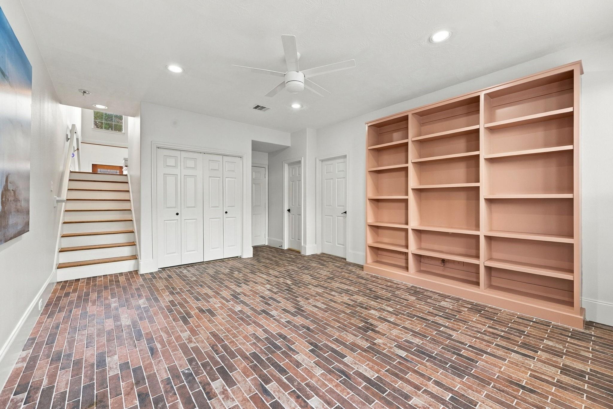 Empty room with brick flooring, a staircase, and built-in peach-colored shelving.