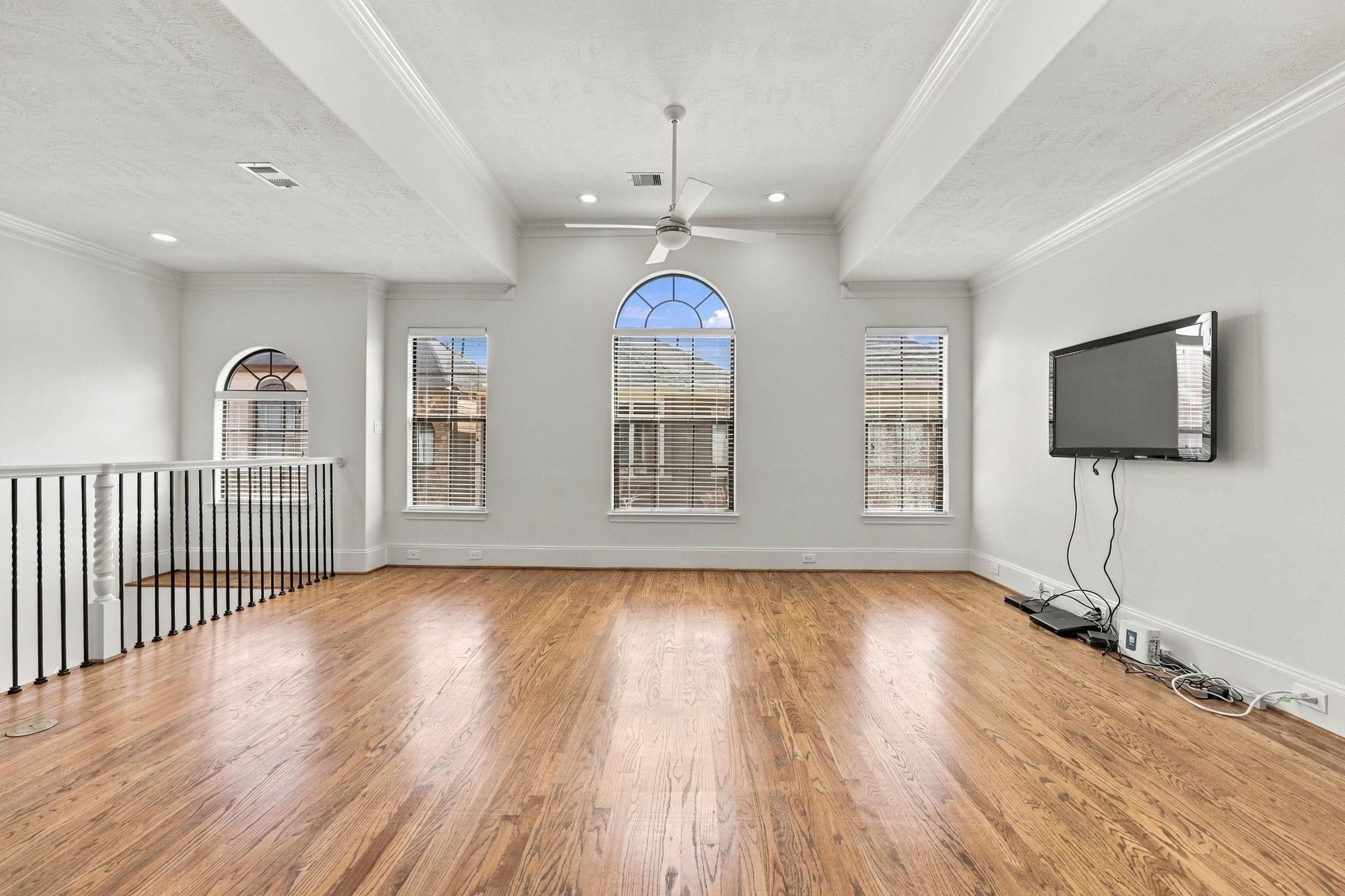 Living area with hardwood floors, arched windows, a high ceiling, and a stair railing.