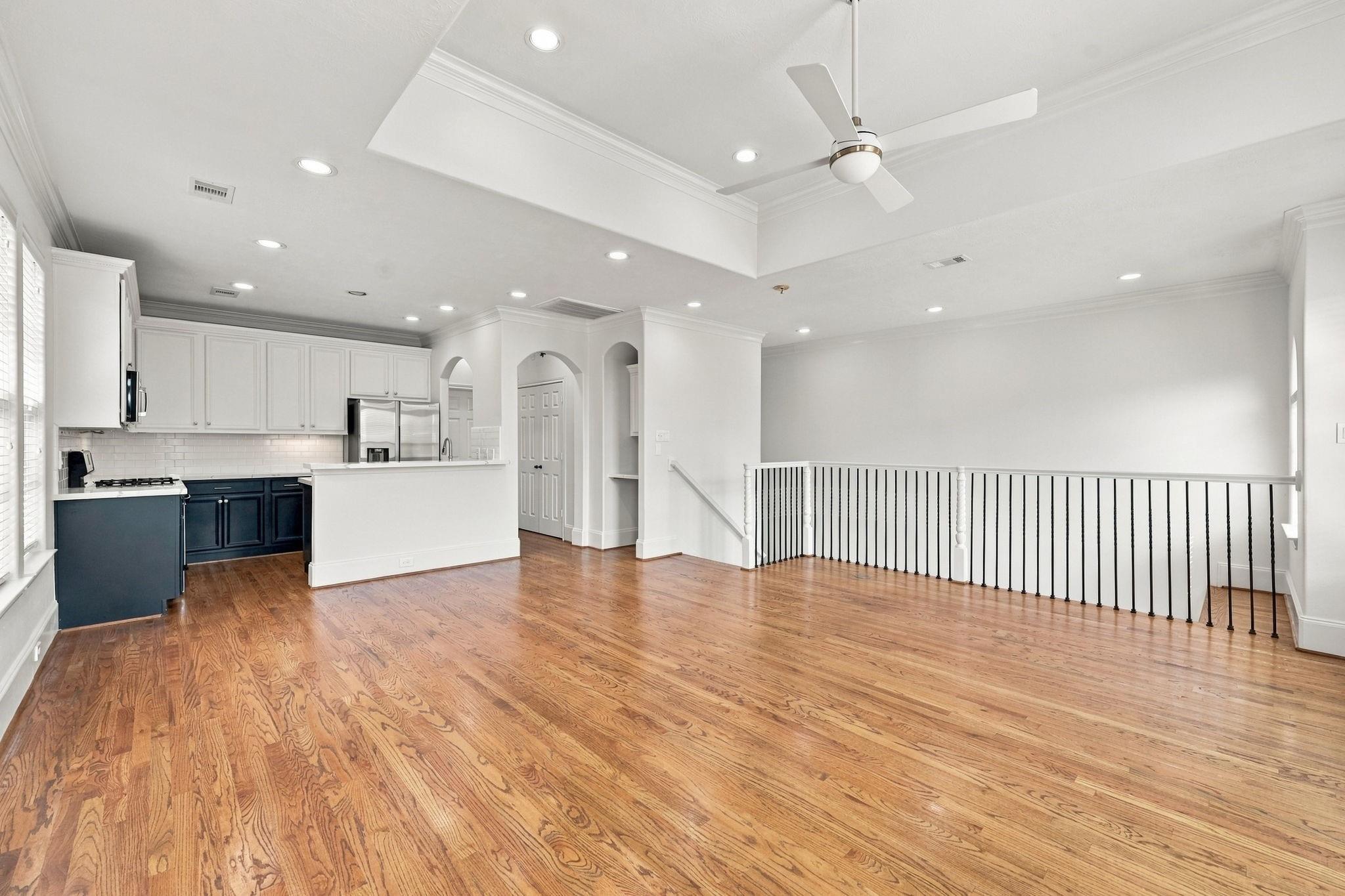 Open-plan kitchen and living area with dark blue cabinets, hardwood floors, and a railing around the stairwell.