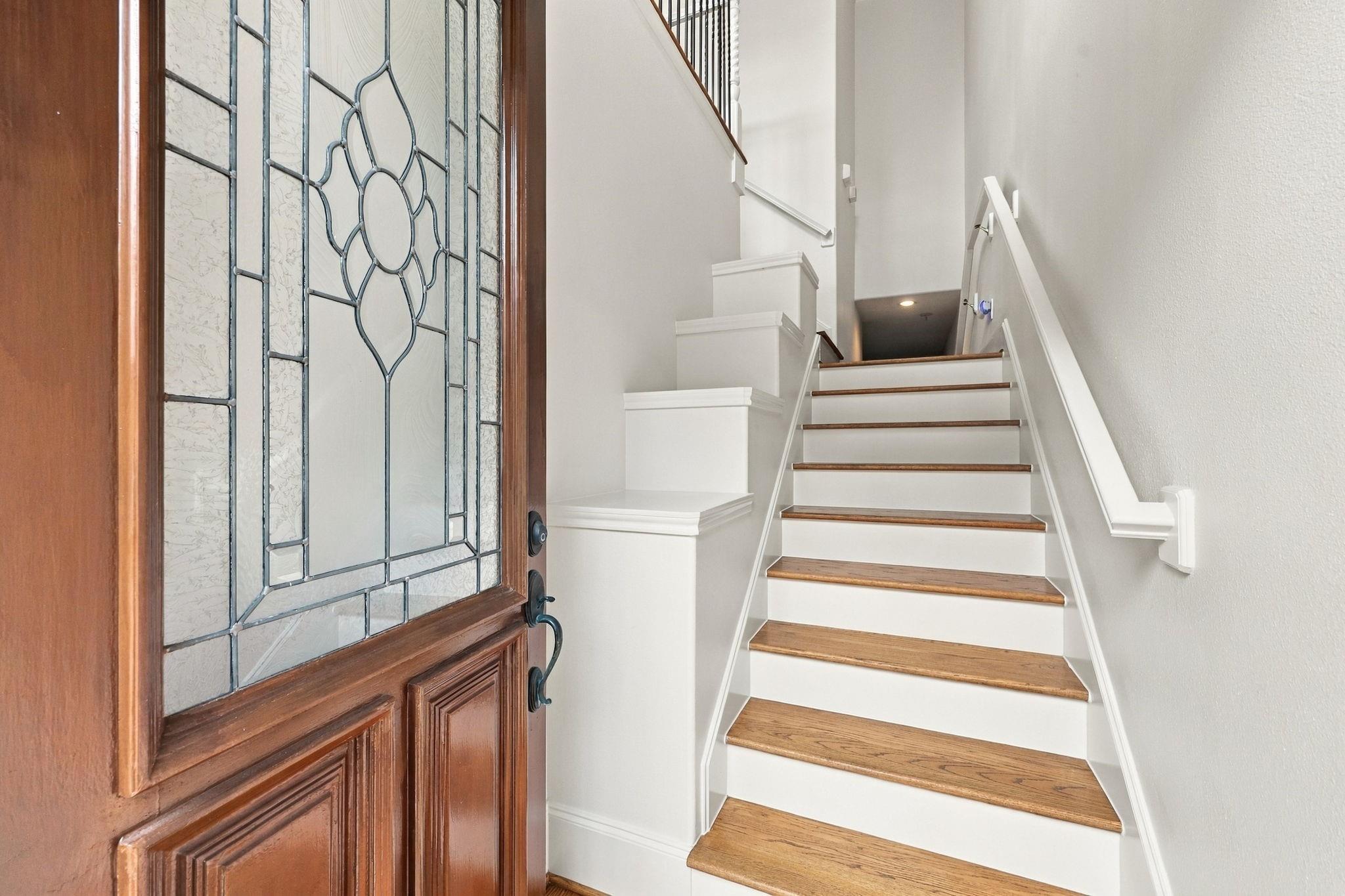 Entryway staircase with wood treads beside a decorative glass-paneled wood front door.