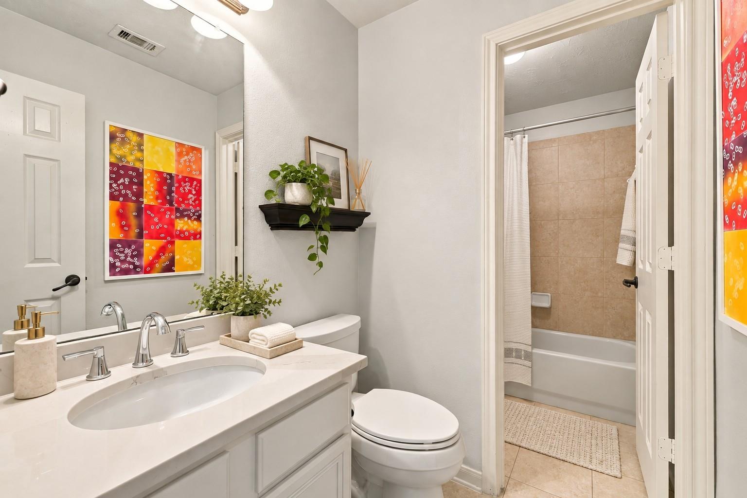 Bathroom with white vanity and toilet beside a tiled bathtub and shower.