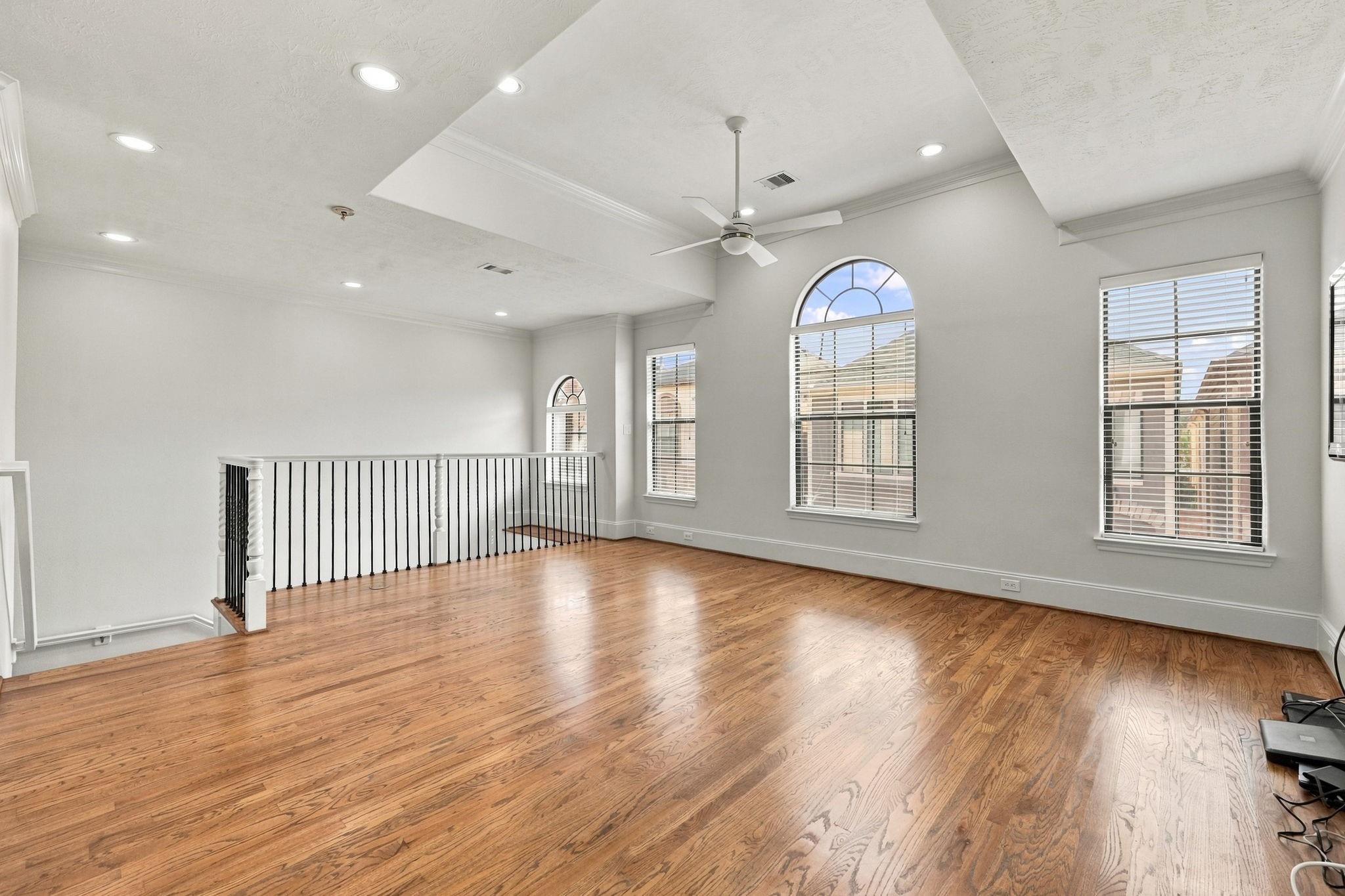 Vacant upper-level living area with hardwood floors, black stair railing, and tall arched windows.