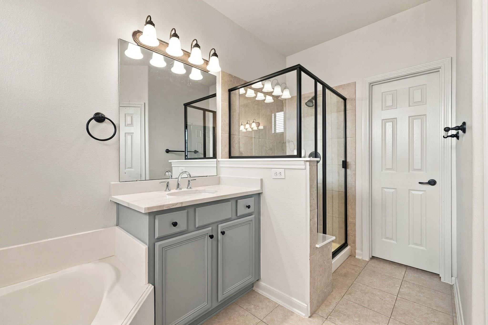 Bathroom with gray vanity, glass-enclosed tiled shower, and bathtub.