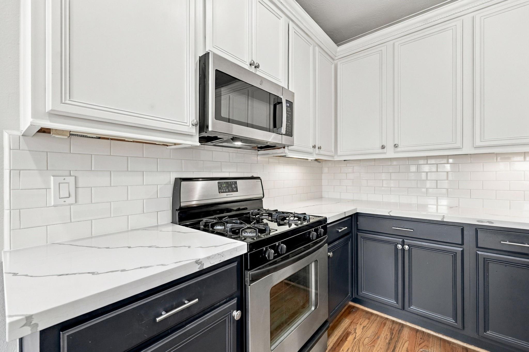 Kitchen with navy lower cabinets, white veined countertops, and a stainless steel gas range.