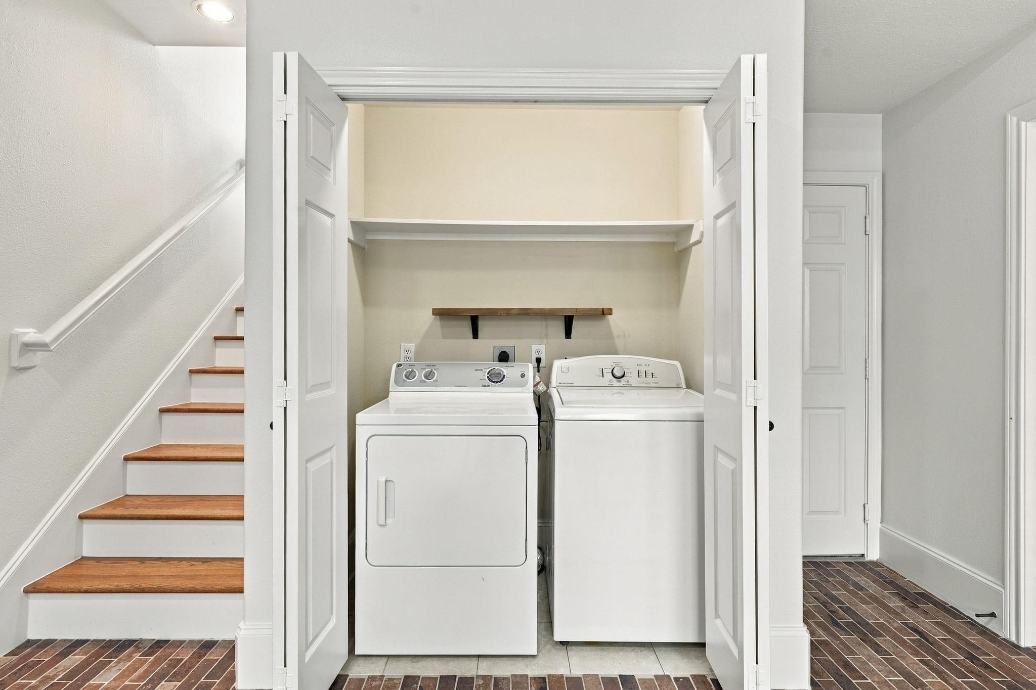Washer and dryer in an open closet beside a staircase with wood treads.