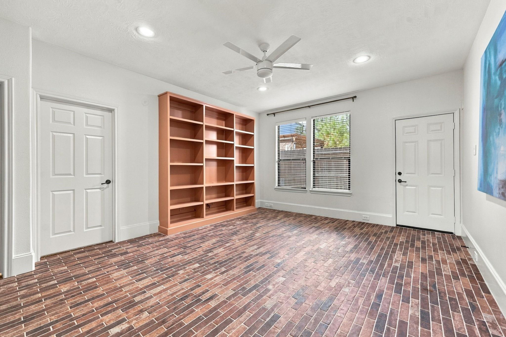 Empty room with built-in shelving, brick flooring, two doors, and a ceiling fan.