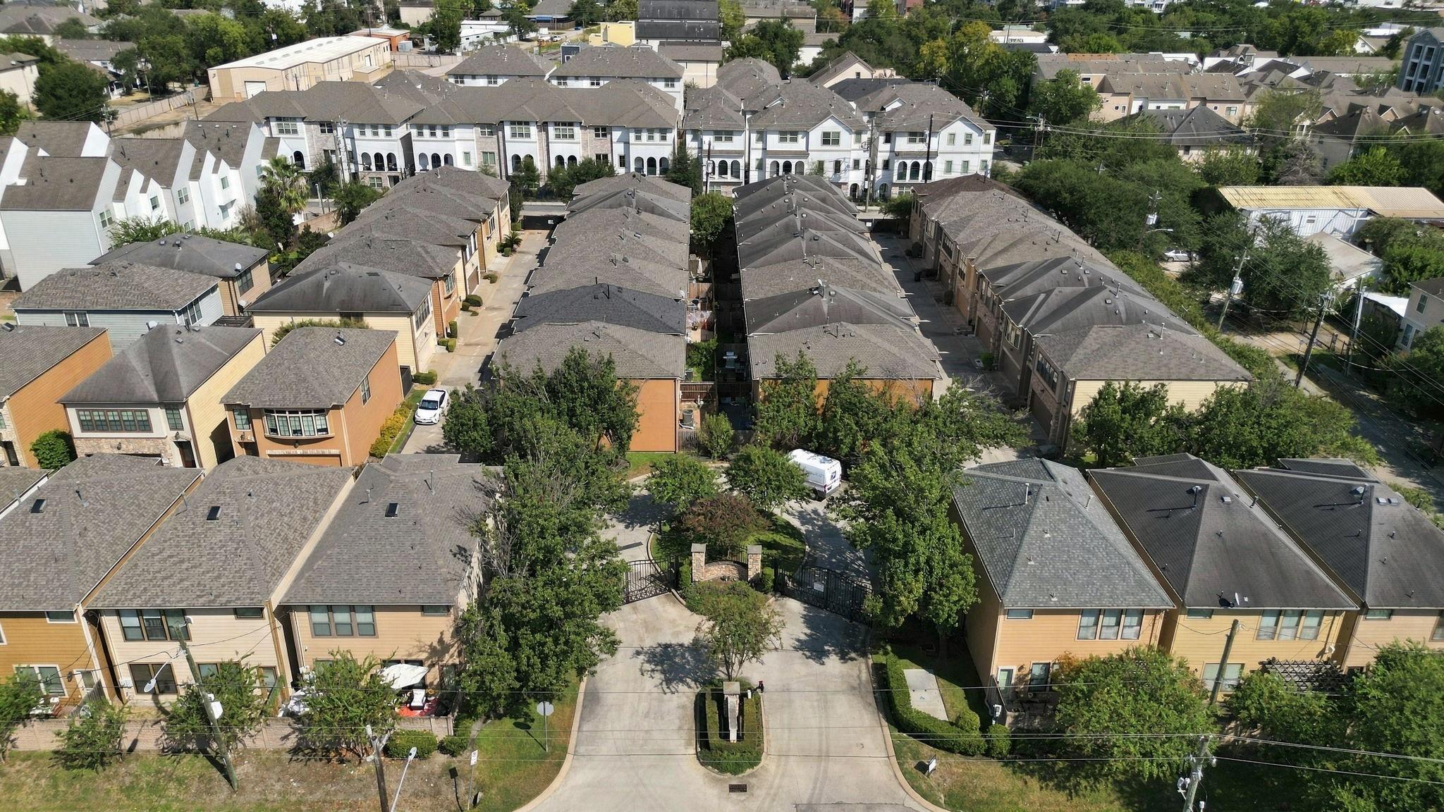 Aerial view of a gated townhome community with rows of homes and tree-lined driveways.