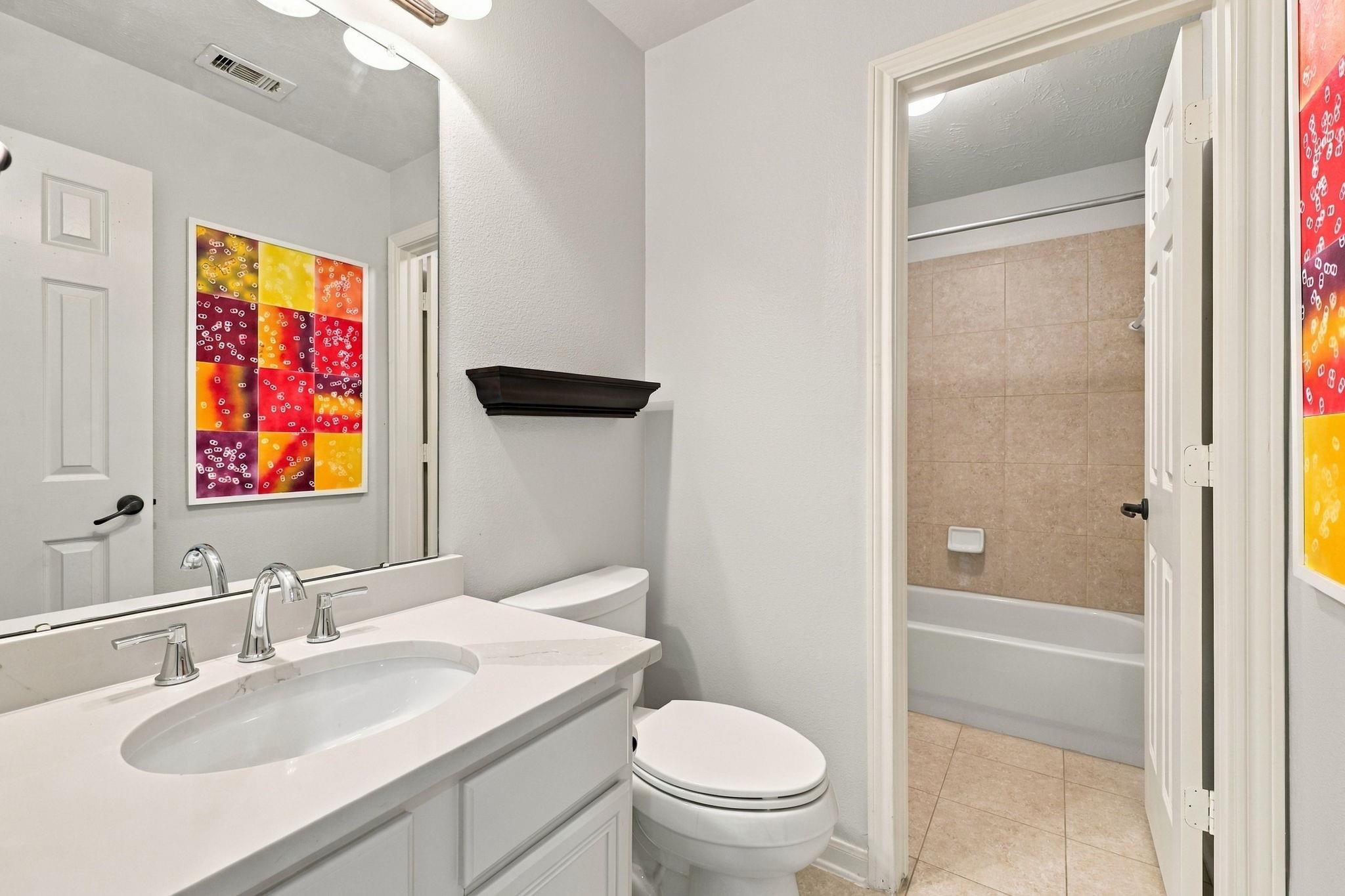 Bathroom with a white vanity, toilet, and bathtub with a tan tiled surround.
