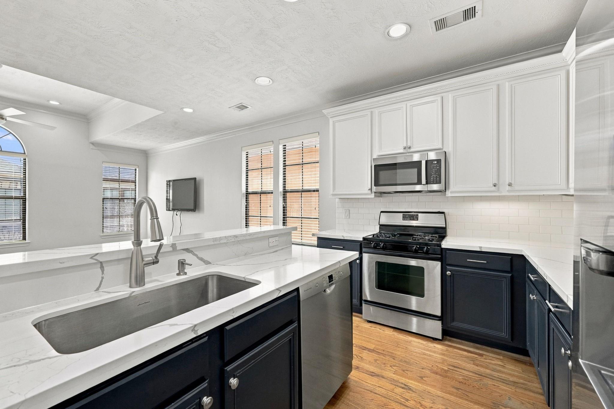 Kitchen with navy cabinets, veined white counters, a large stainless sink, and stainless appliances.