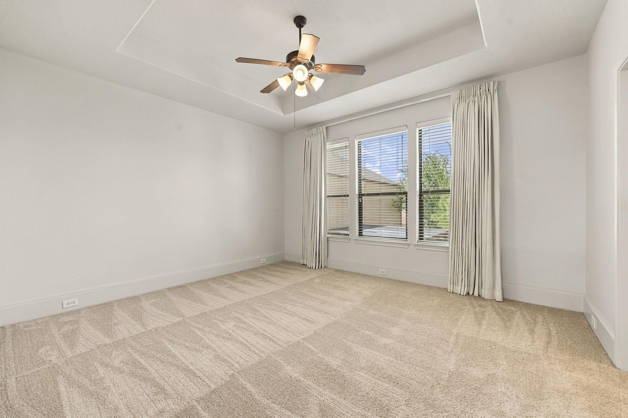Empty carpeted bedroom with a ceiling fan and three curtained windows.
