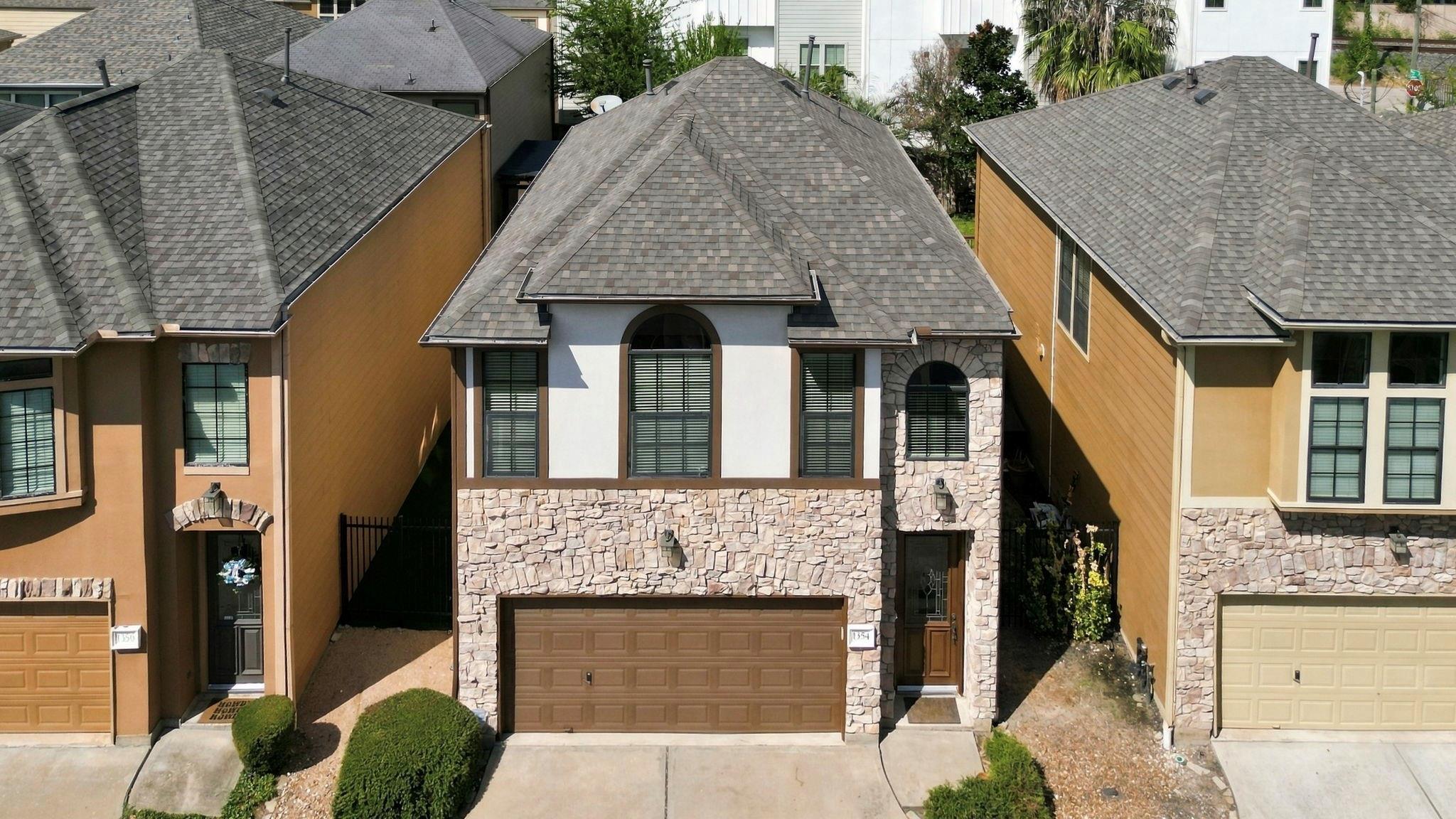 Townhouse with a stone facade, arched windows, and a double garage, viewed from above.