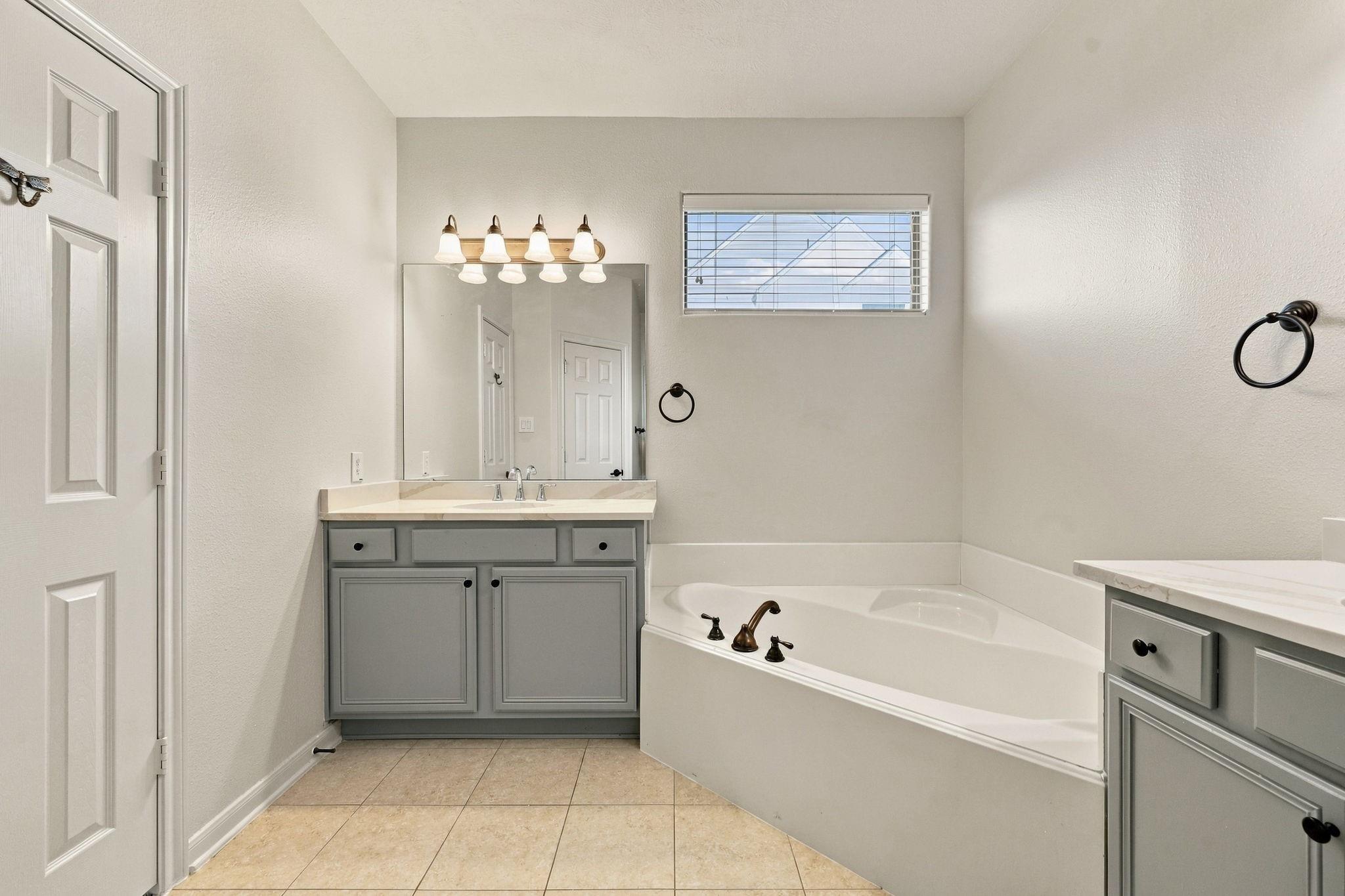 Bathroom with a built-in tub, gray vanity, wide mirror, and window with blinds.