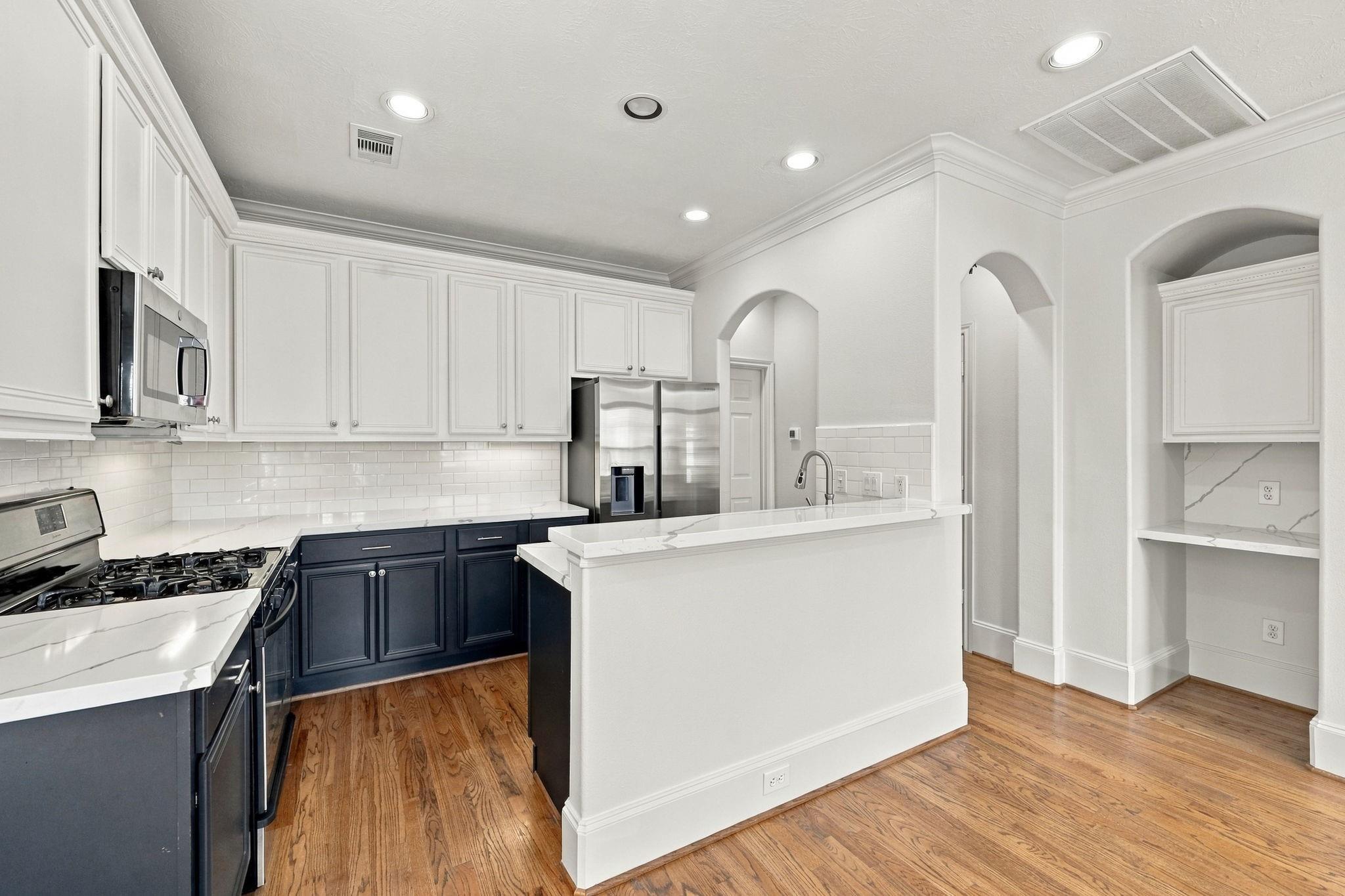 Kitchen with a white island, dark blue lower cabinets, stainless steel appliances, and hardwood floors.