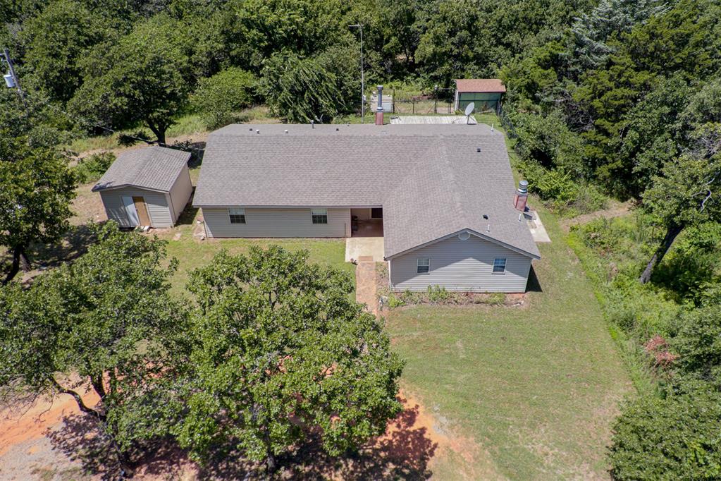 Aerial view of a single-story house and detached shed among mature trees.