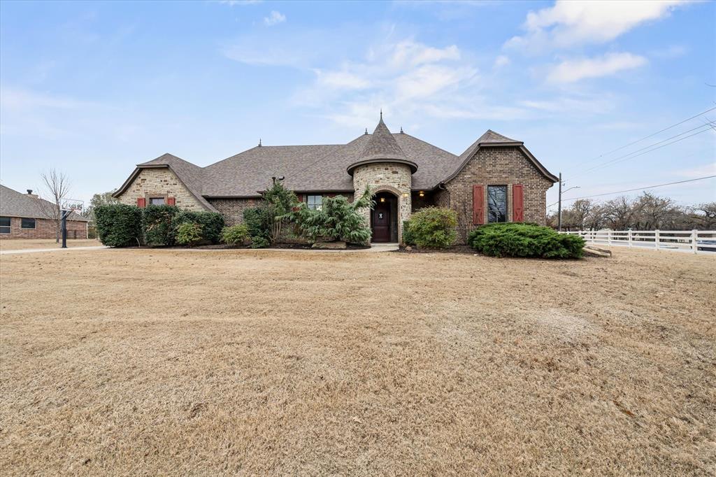 Brick house with a round entry turret, red shutters, and a large lawn.
