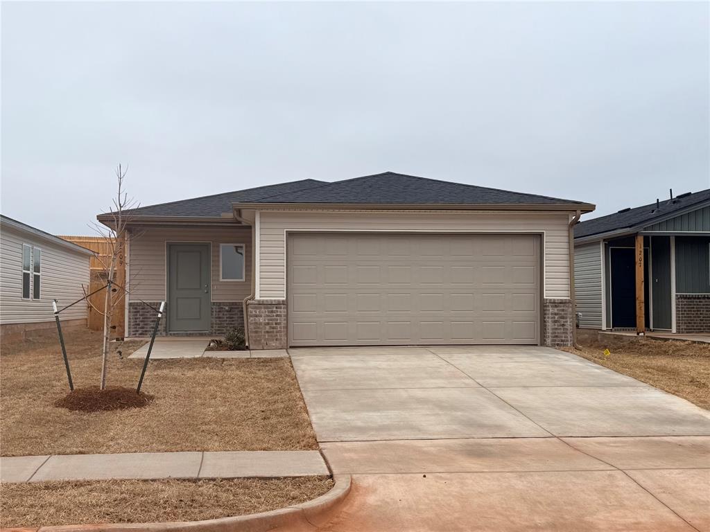 Single-story beige house with a double garage, brick accents, and a wide concrete driveway.