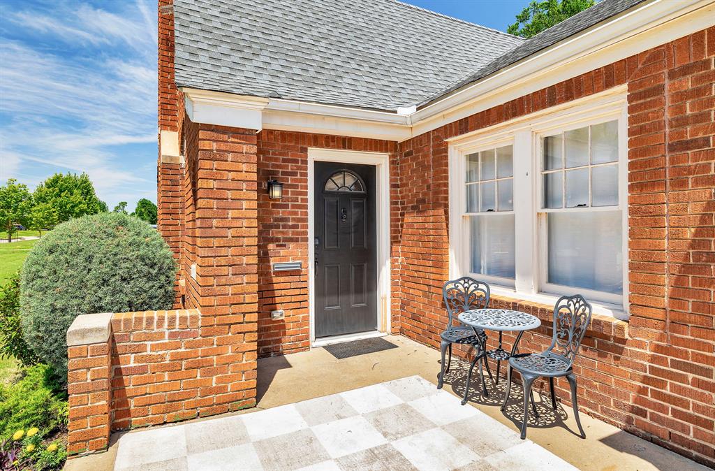 Red-brick house entrance with a dark arched door and a small patio with metal seating.