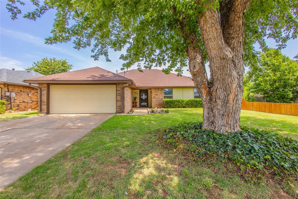 Single-story brick home with a two-car garage partly framed by a large front-yard tree.