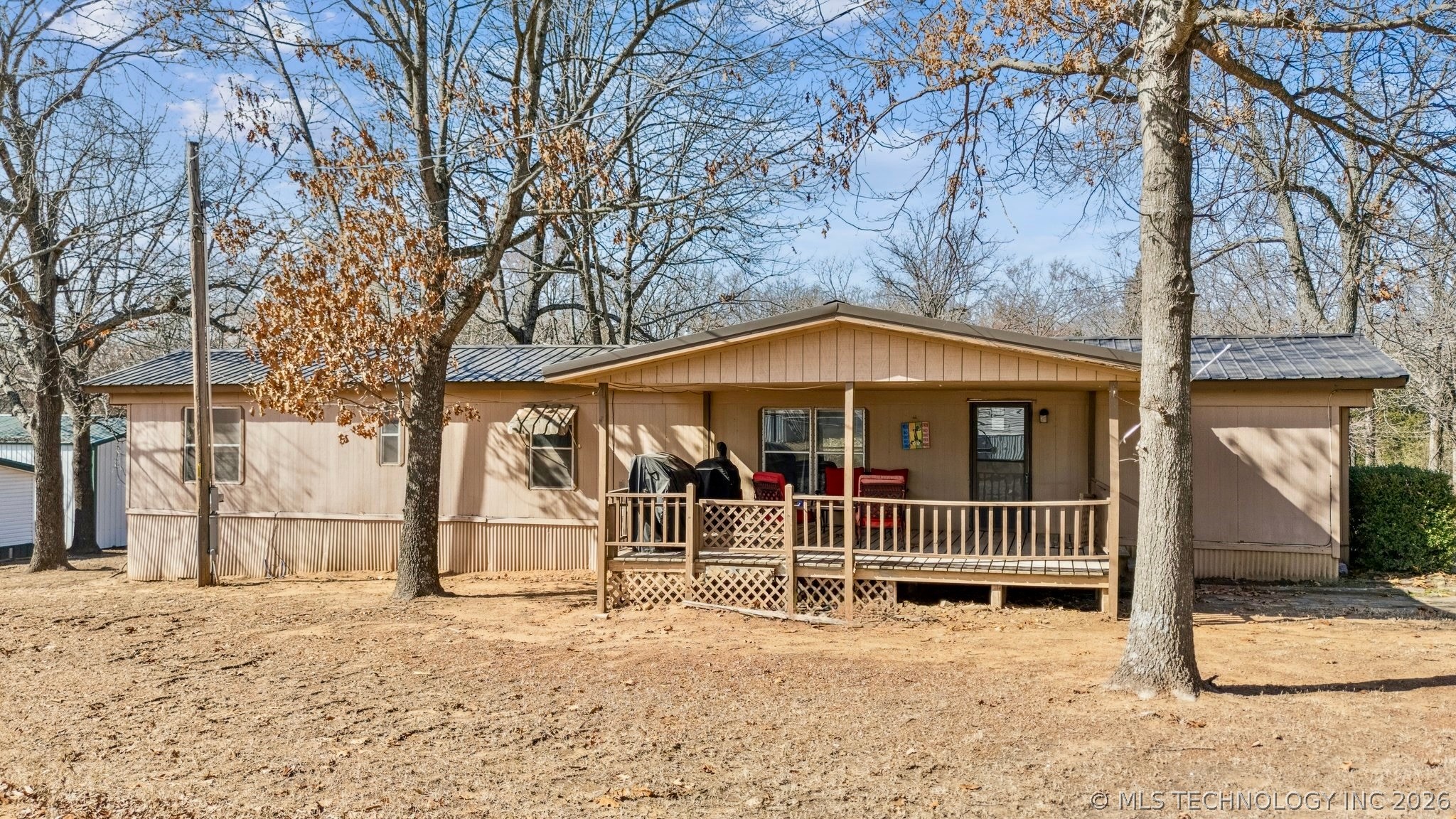 Single-story manufactured home with a covered porch, red chairs, and leafless trees in the front yard.