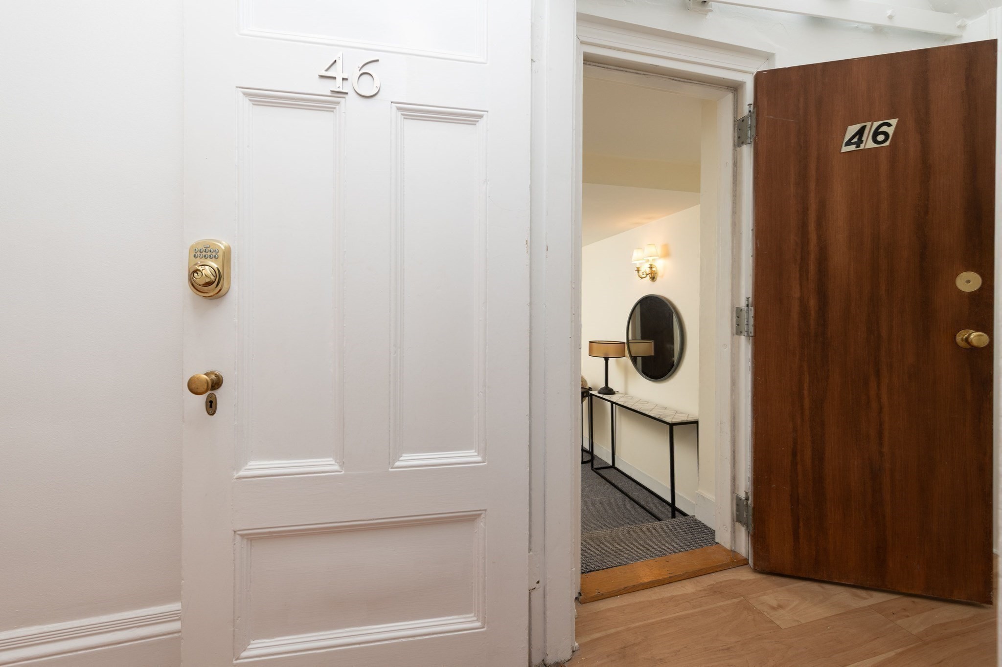 Unit 46 entry with a brass keypad lock and a foyer console table, oval mirror, and wall sconce.