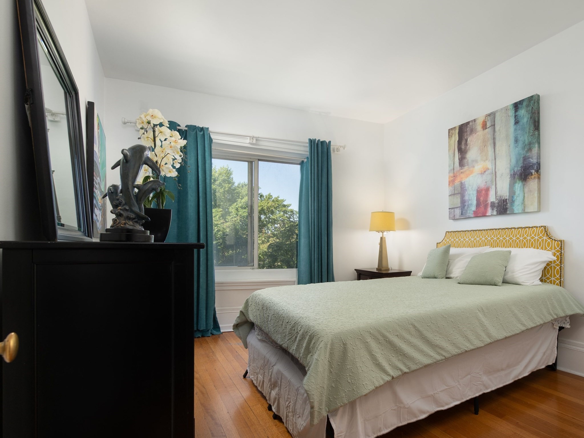 Bedroom with a large bed, teal curtains, and a window overlooking trees.