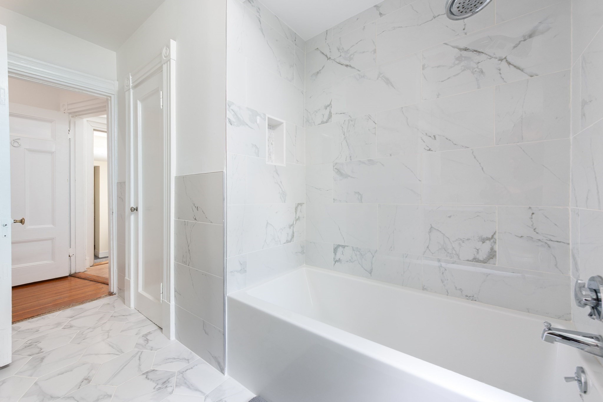 Renovated bathroom with a white bathtub, marble-look tile, and a recessed shower niche.