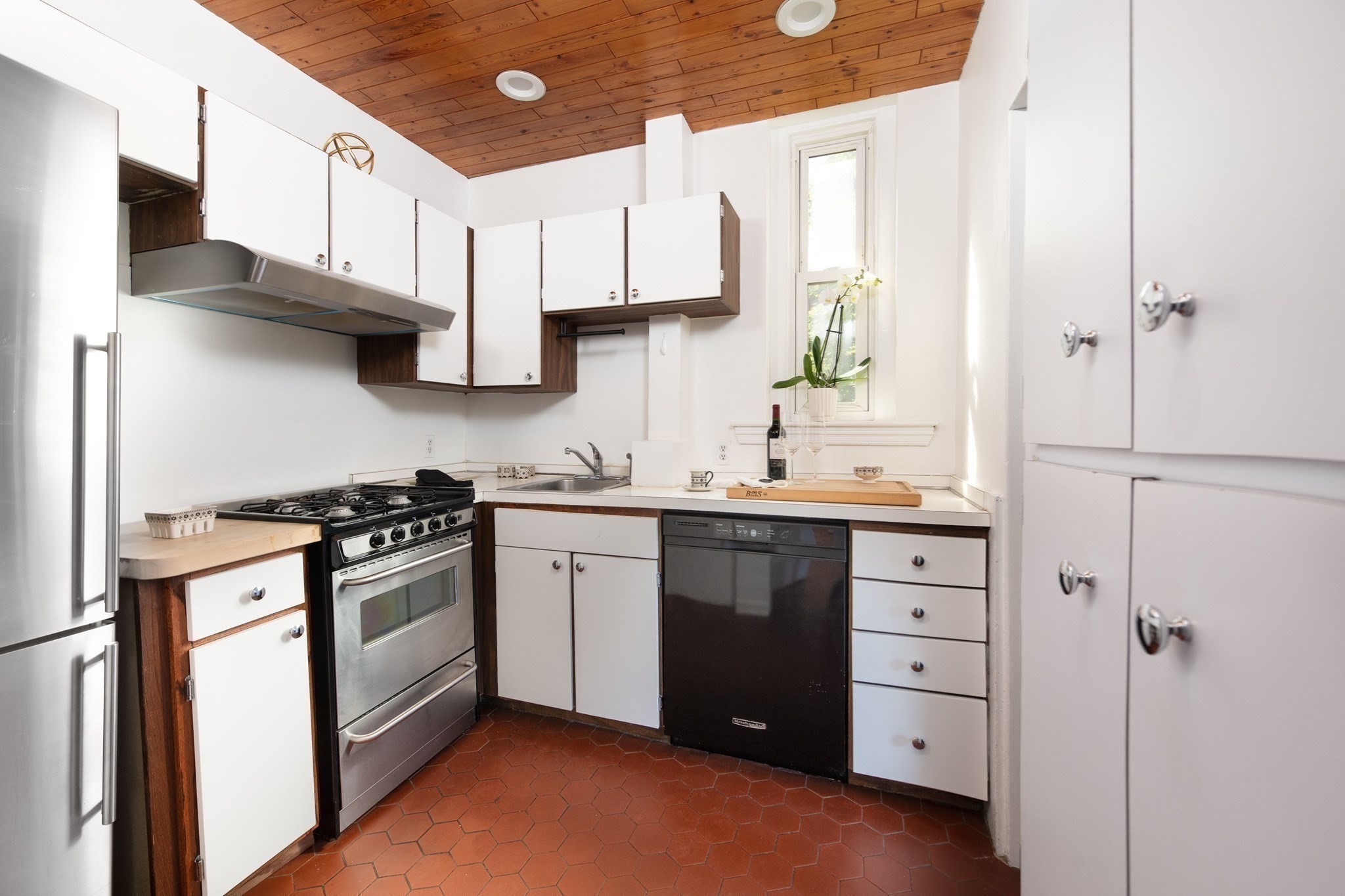 Kitchen with white and dark wood cabinets, terracotta tile floor, and a wood-plank ceiling.