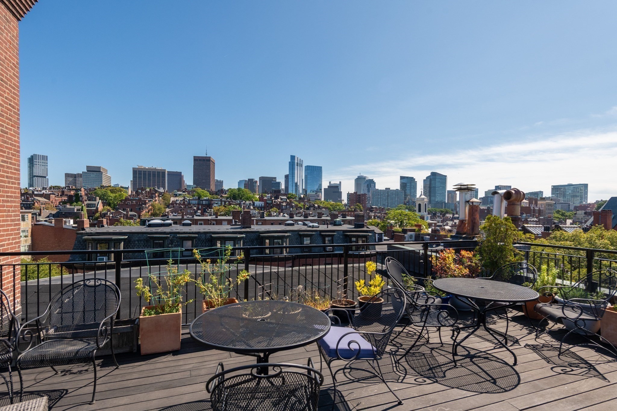 Rooftop deck with metal patio furniture, planters, and a wide Boston skyline view.