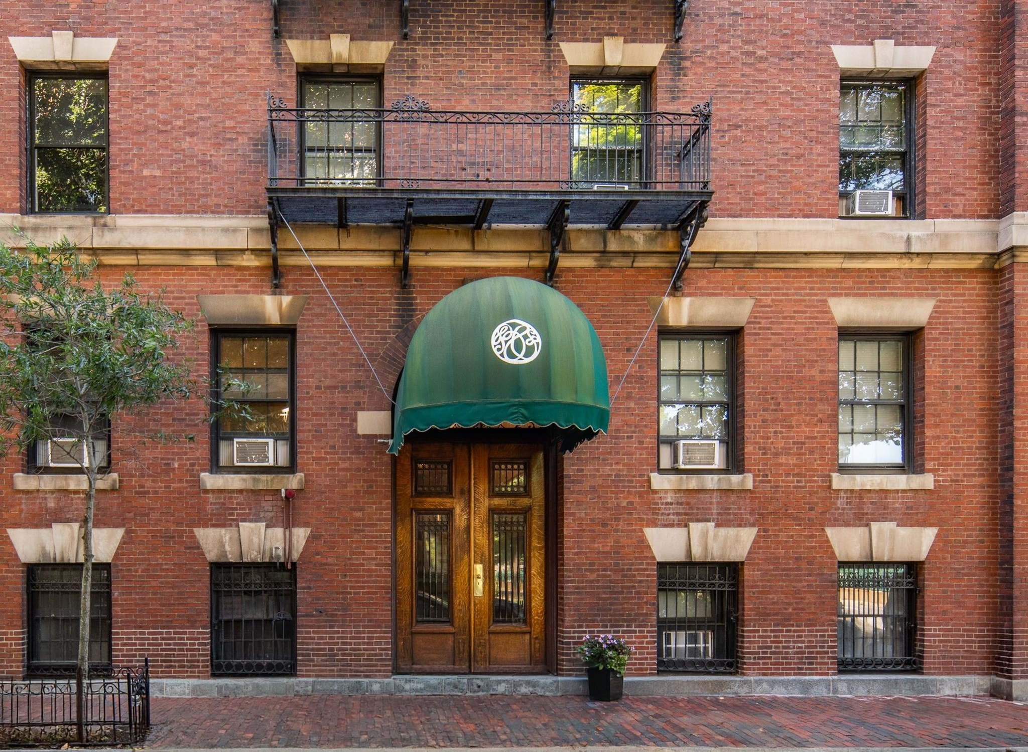 Red-brick building entrance with a green arched awning, ornate wooden doors, and an iron balcony.