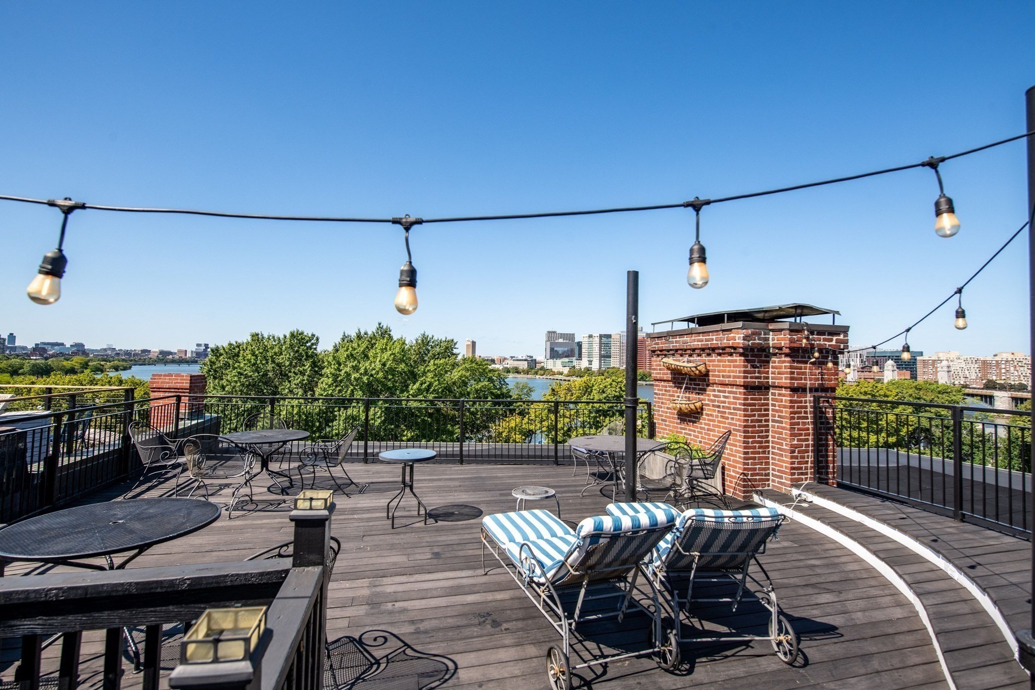 Rooftop deck with striped lounge chairs, string lights, and views of water and the Boston skyline.