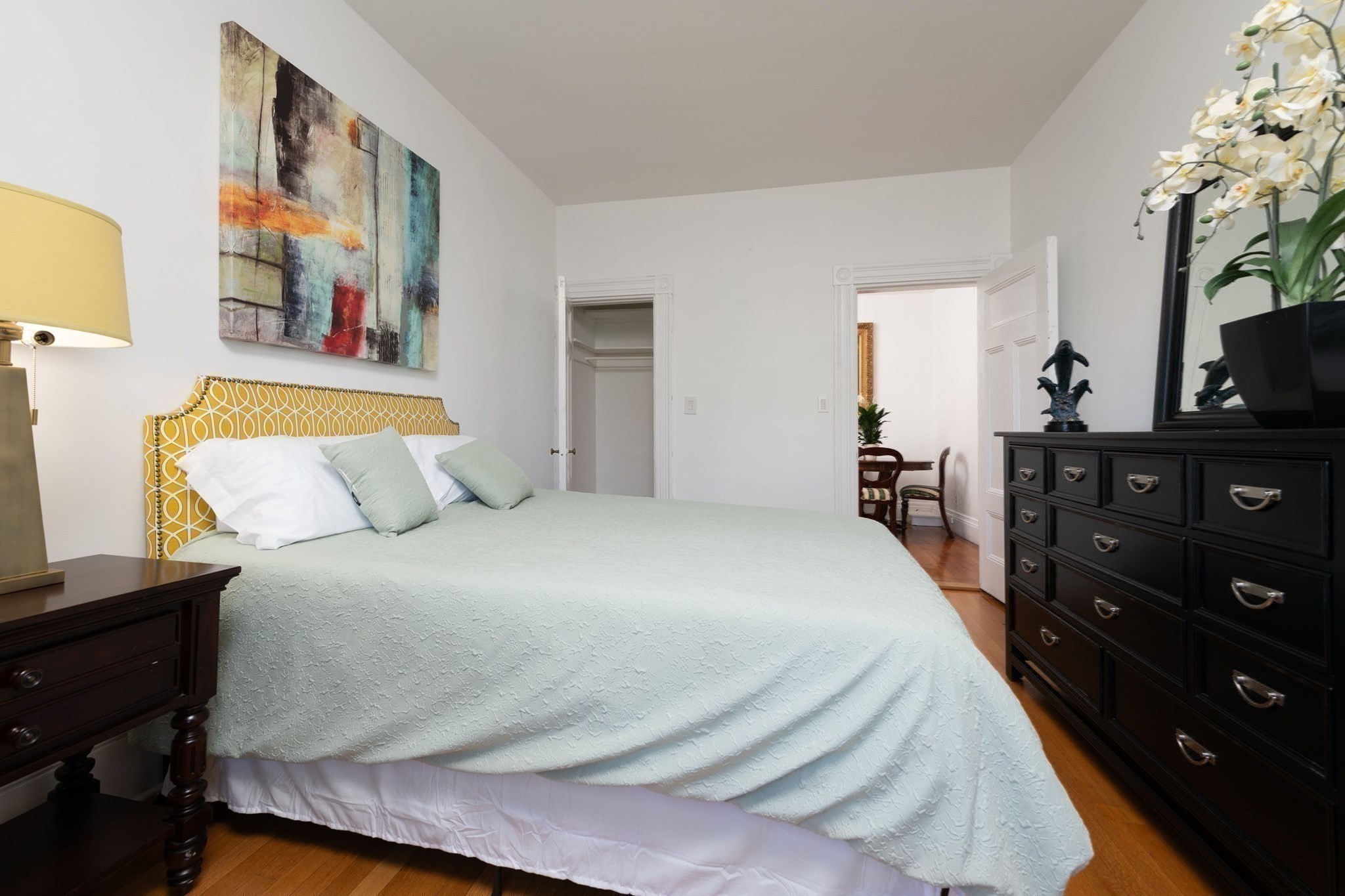 Staged bedroom with mint bedding, a yellow patterned headboard, and dark wood dressers.