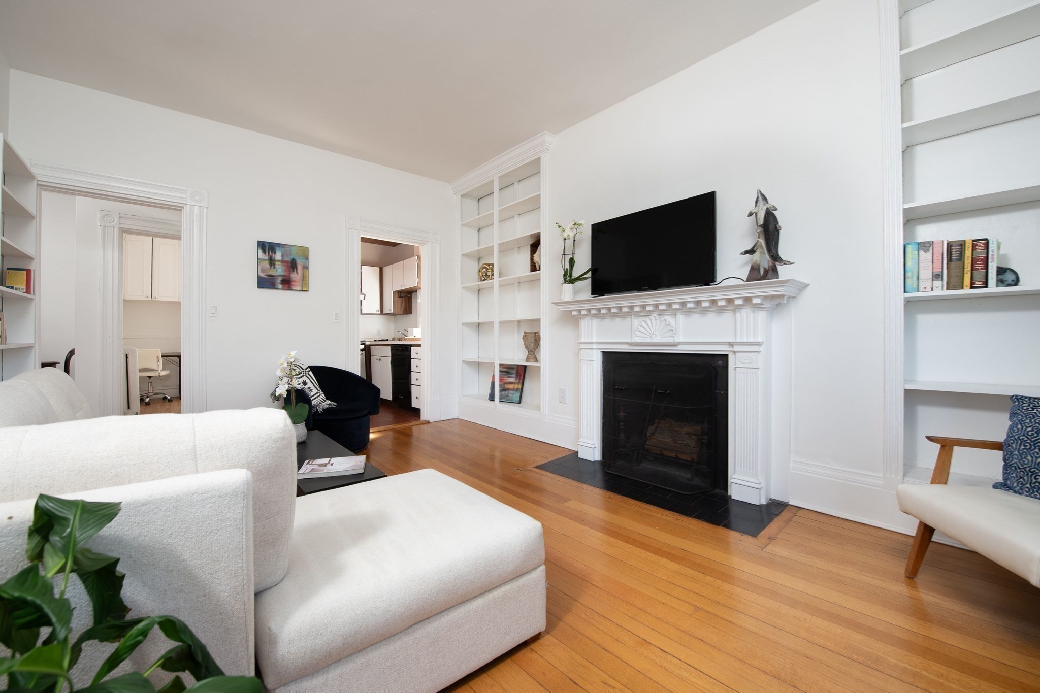 Living room with a white sofa, hardwood floors, and a white fireplace beneath a television.