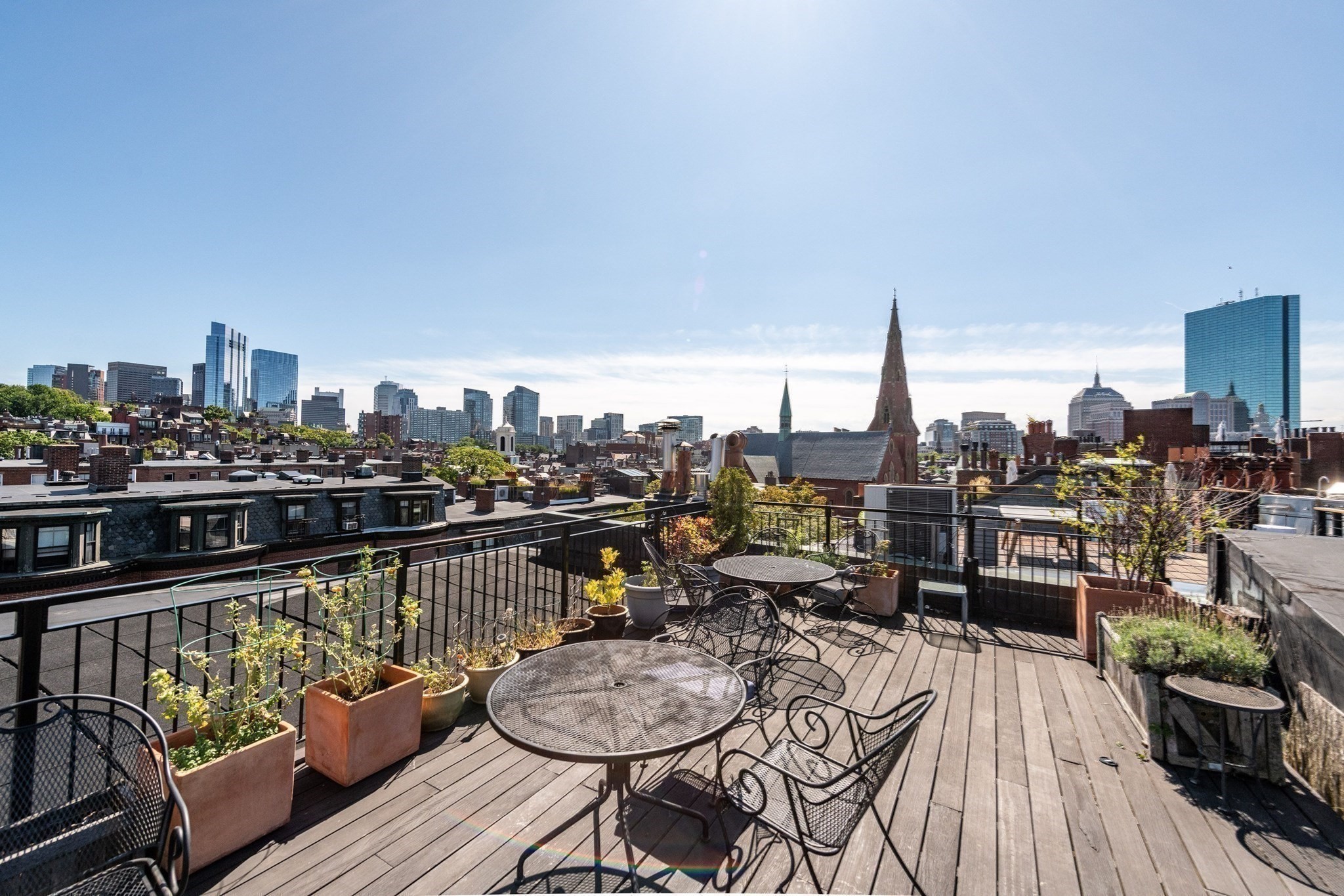 Rooftop deck with café furniture and planters overlooking Boston’s skyline.