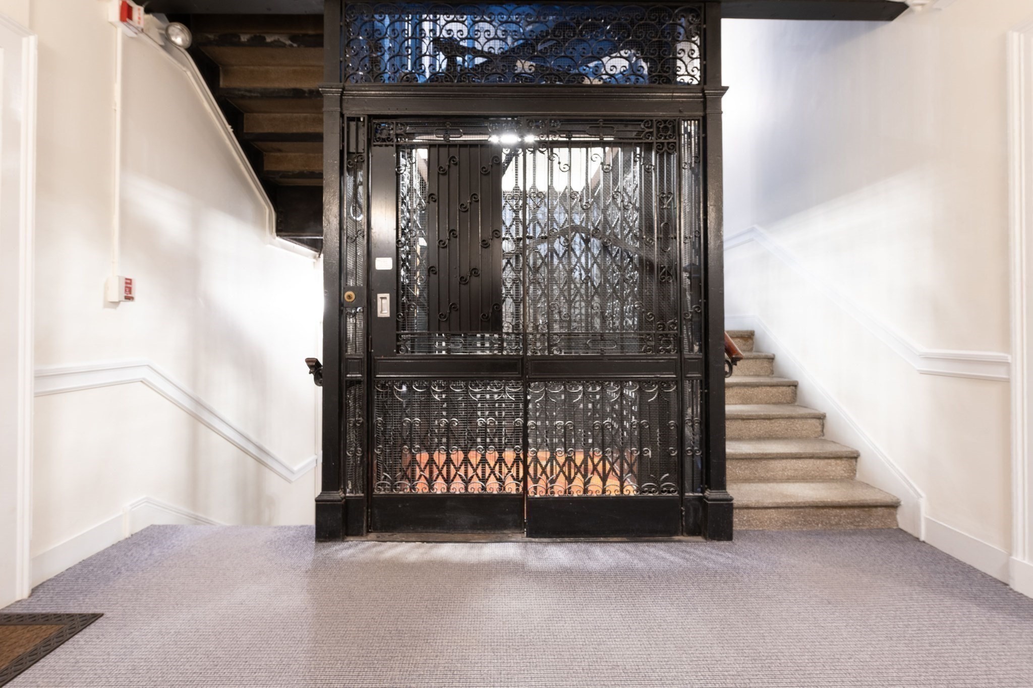 Ornate wrought-iron elevator cage between carpeted staircases in a bright entry hall.