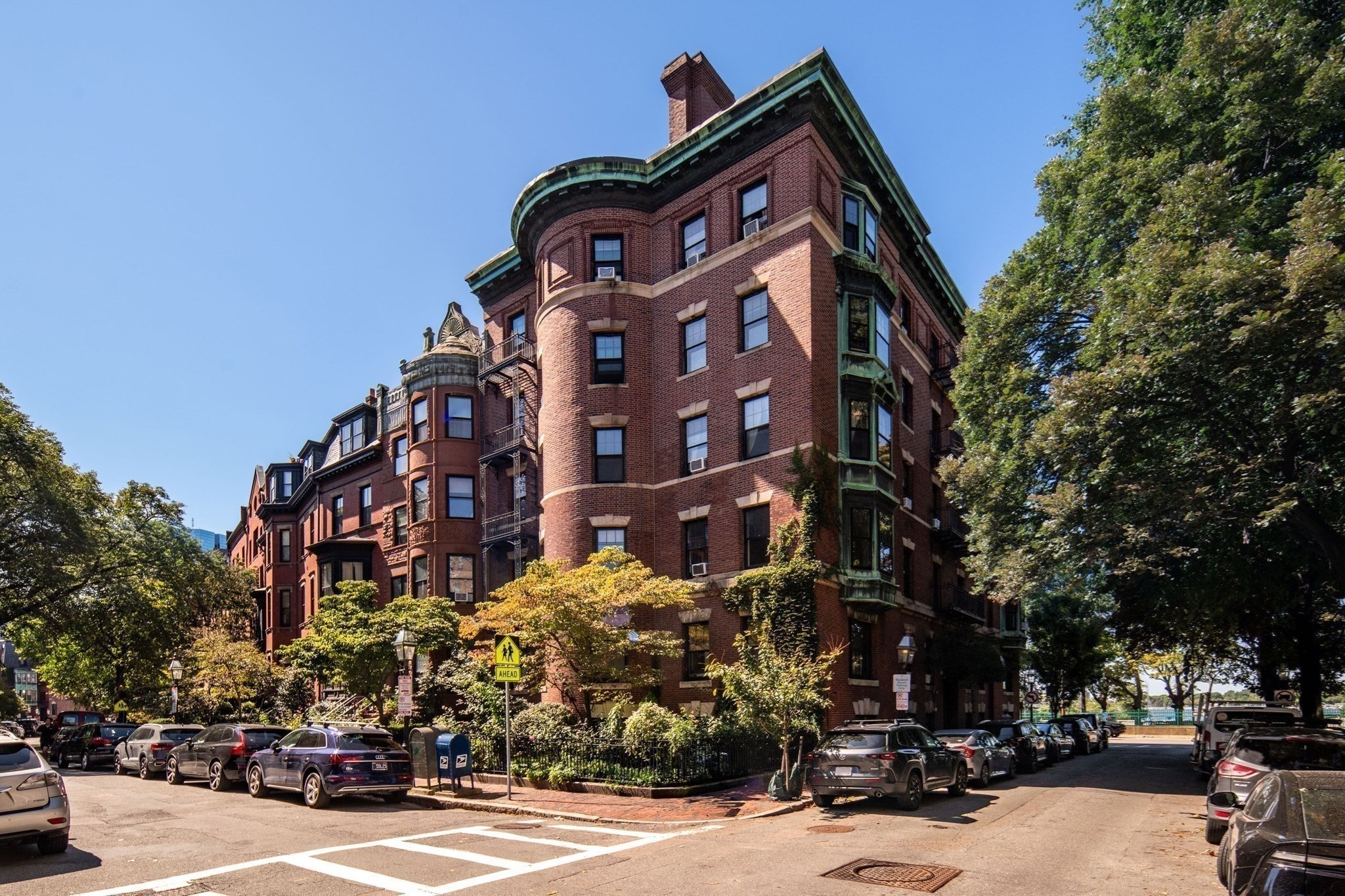 Red-brick residential building with rounded bay windows and green trim on a tree-lined street.