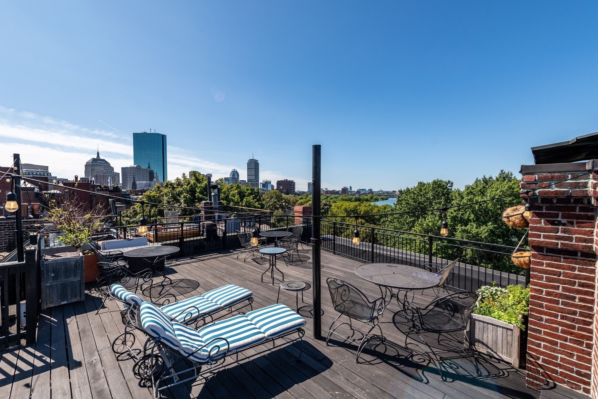 Rooftop deck with striped loungers and café tables overlooking the Boston skyline and water.