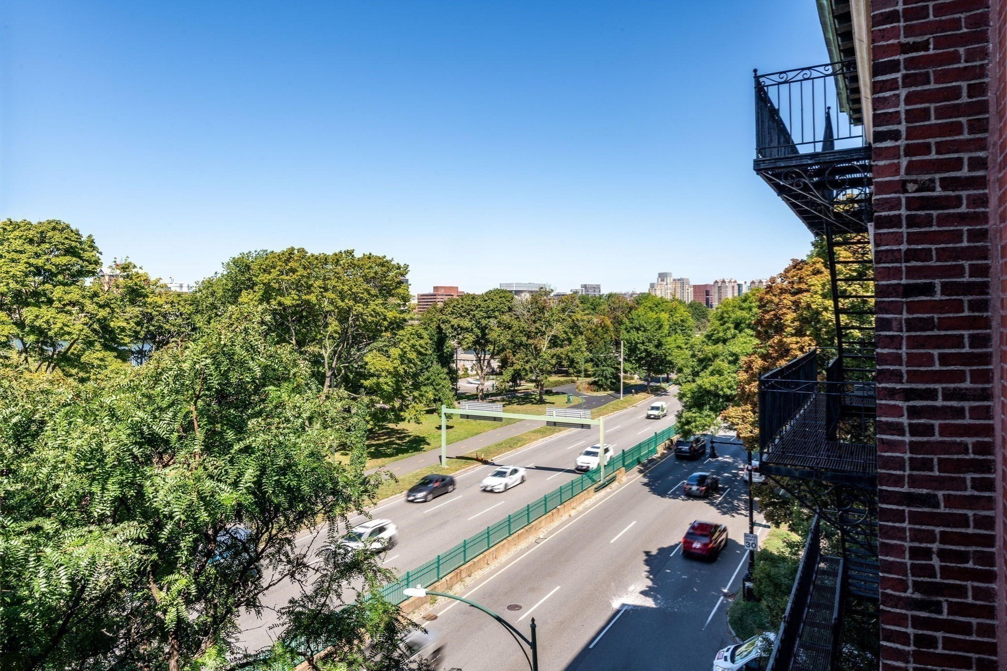 View over a leafy park and busy road from beside a brick building with metal fire escapes.