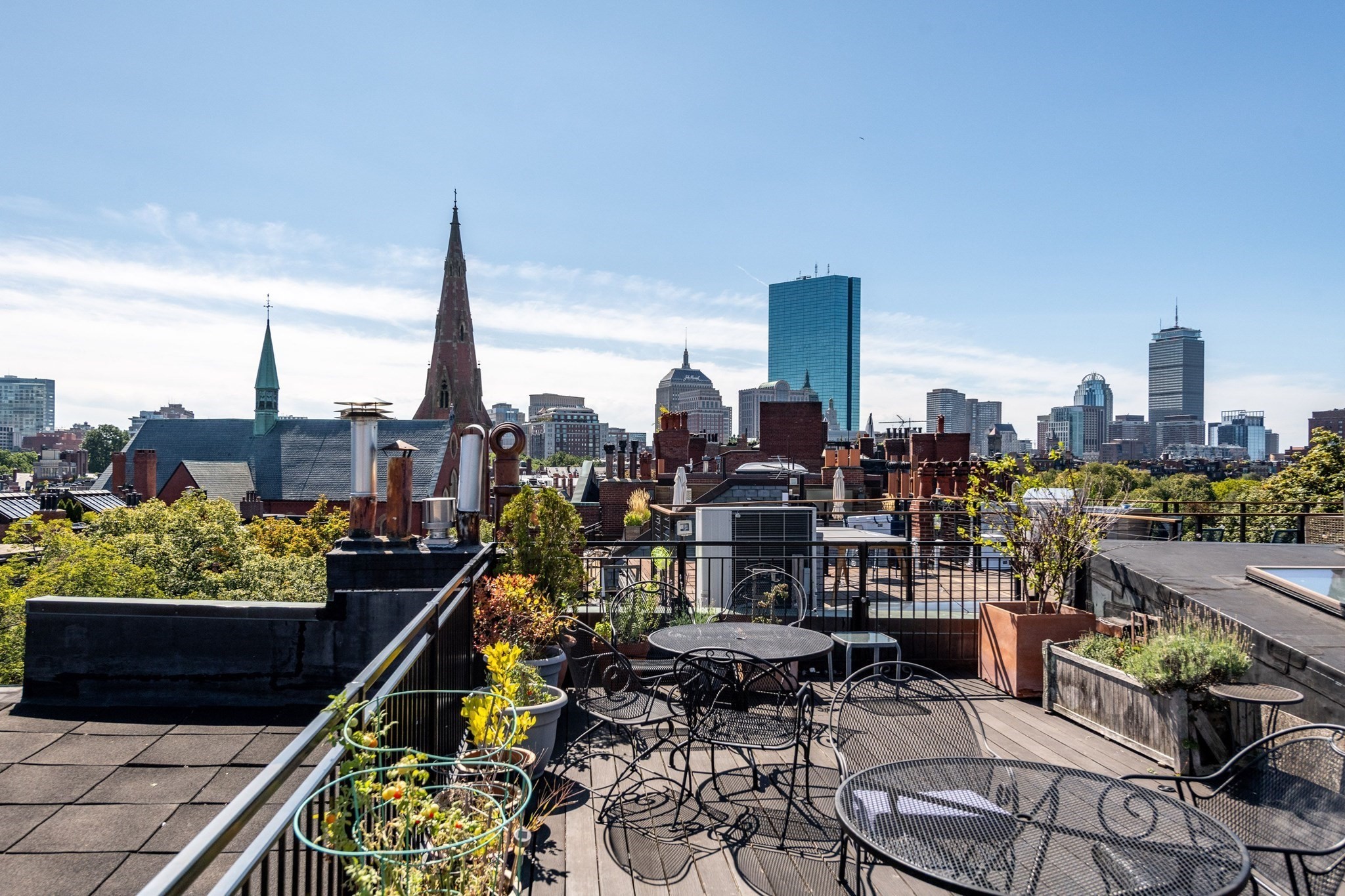 Rooftop terrace with patio seating and potted plants overlooking the Boston skyline.