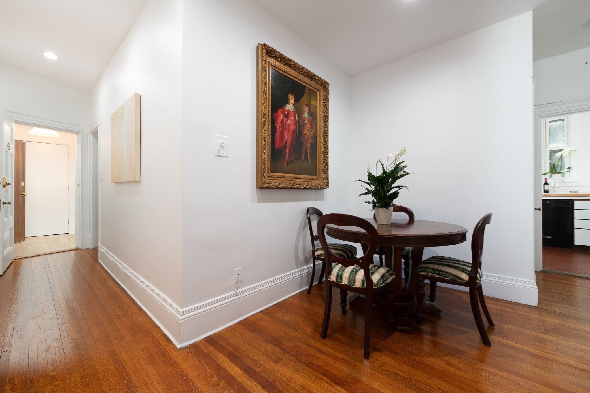 Dining area with a round wooden table, ornate framed painting, and hardwood floors.