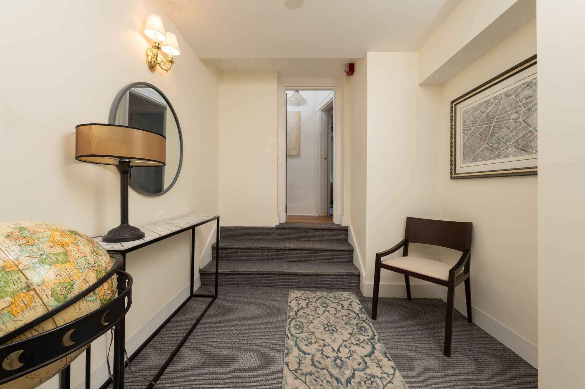 Apartment entry hall with carpeted steps, a globe on a console, and a chair beside a patterned runner.