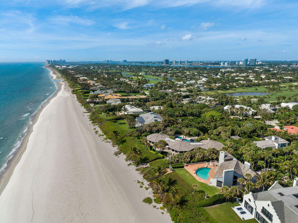Aerial view of beachfront homes and a sandy shoreline, with a backyard pool and distant high-rises.