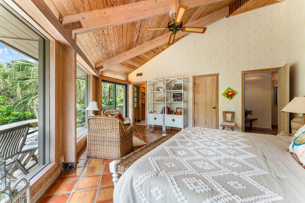Bedroom with a vaulted wood ceiling, terracotta tile, wicker chairs, and windows facing tropical greenery.